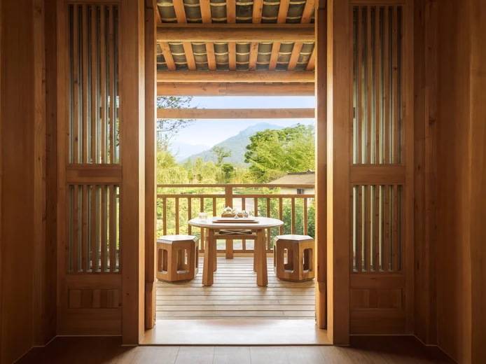 A balcony with a round table and four stools faces green trees and distant mountains, offering open sky views for a tranquil, nature-connected experience.