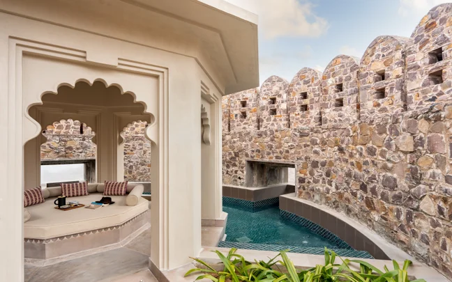 An outdoor lounge with arched features faces a stone wall and private pool, thoughtfully combining traditional forms with modern design elements.