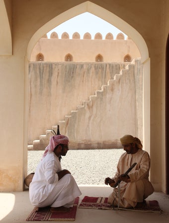 Khách thư giãn trên những tấm thảm dệt tay dưới bóng râm của một cánh cửa vòm, nhìn ra một sân trong ngập tràn ánh nắng và những bậc thang đá, gợi lên di sản địa phương và không gian yên bình.
