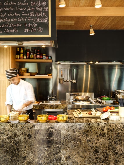 Un expert culinaire prépare des ingrédients frais sur un comptoir en marbre dans une cuisine contemporaine, entouré d'ustensiles et de produits.