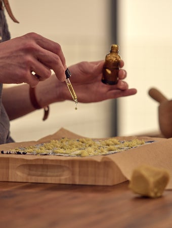 Chất lỏng được đổ từ một chai màu nâu lên phô mai bào trên giấy nến, với một dụng cụ bào và cối xay gần đó trên một chiếc bàn gỗ.