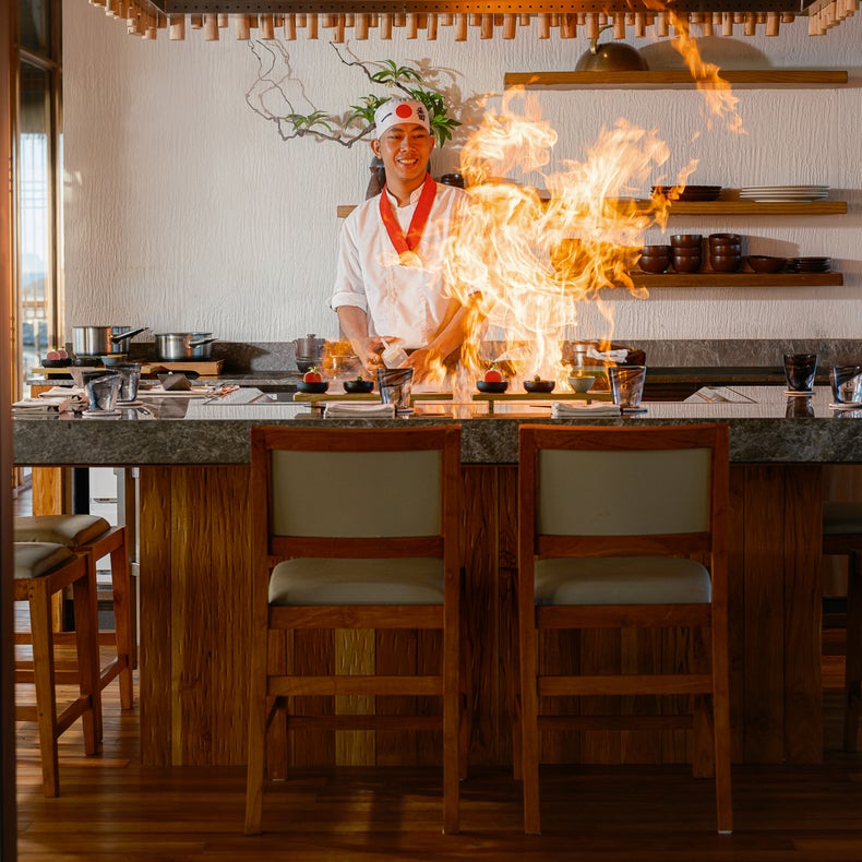 A person prepares fresh seasonal ingredients at a kitchen counter, reflecting wellness and sustainable cooking practices in a thoughtfully designed space.