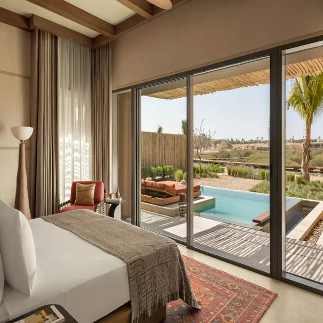 Bedroom with floor-to-ceiling glass doors opens to a private patio, featuring a pool and lounge chairs overlooking a sunlit, thoughtfully landscaped garden.