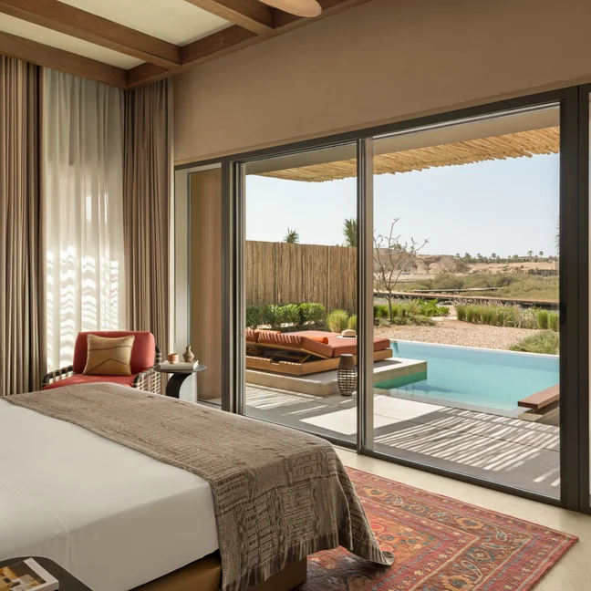 Bedroom with floor-to-ceiling glass doors opens to a private patio, featuring a pool and lounge chairs overlooking a sunlit, thoughtfully landscaped garden.