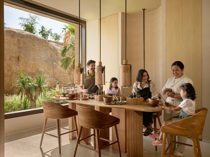 Guests participate in a wellness activity at a wooden table near sunlit windows, overlooking desert landscapes and palm trees.