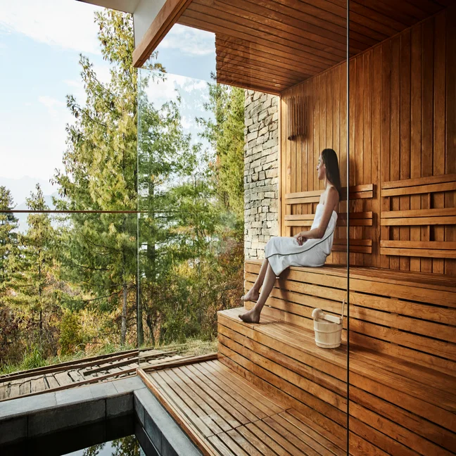 El huésped disfruta de una sesión de sauna en unos cómodos bancos de madera, con amplios ventanales que ofrecen unas tranquilas vistas de los árboles y el paisaje natural que lo rodean.