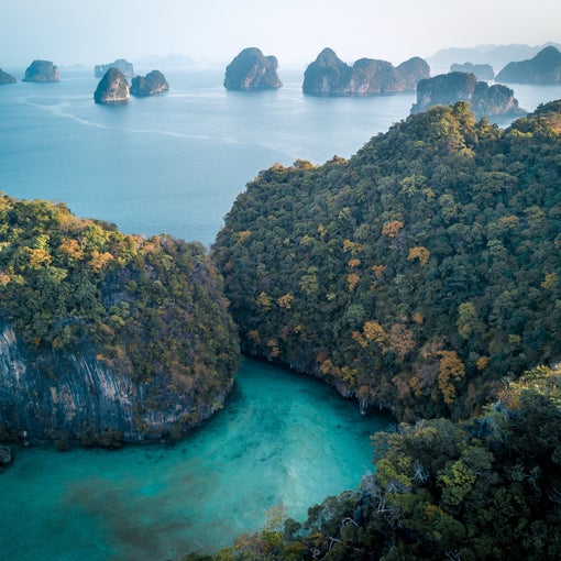 绿树成荫的岛屿被碧绿的海水环绕,远处是岩石小岛,头顶是柔和迷蒙的天空。.