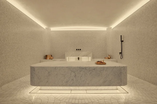 Spacious steam room featuring elegant marble centerpiece, intricate mosaic tiles, gentle lighting, and thoughtfully placed copper fixtures for a serene environment.