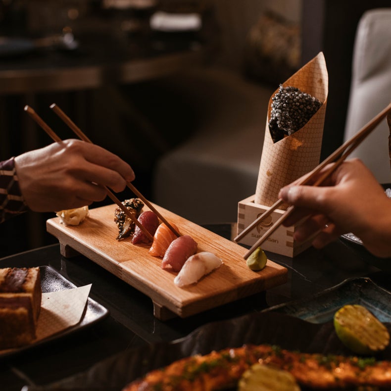 Diners use chopsticks to lift nigiri sushi from a wooden board.