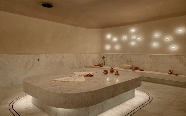 Marble Turkish bath with gentle lighting, copper bowls, and towels arranged on a central stone slab. A tranquil space designed for relaxation and wellbeing.
