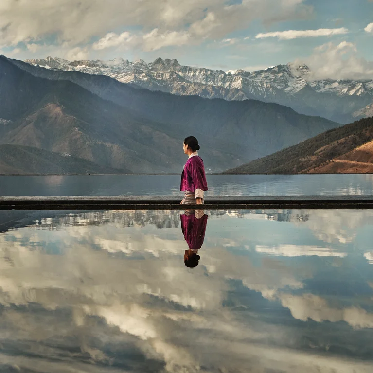 客人身着红色长袍,置身于宁静的泳池边,远处的群山、云雾和雪峰倒影映入眼帘。无障碍环境注重健康和自然。.