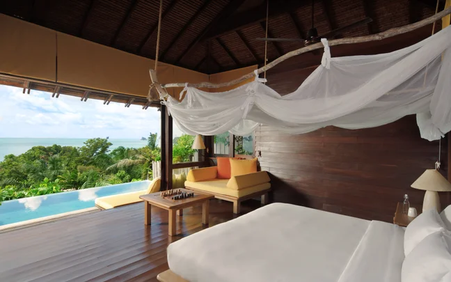 Canopy bed, wooden coffee table with a chess set, and a seating area looking out over a private infinity pool and the ocean.
