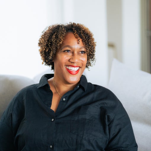 A guest with curly hair sits on a light couch, wearing a black shirt, in a sunlit room designed for comfort and relaxation.