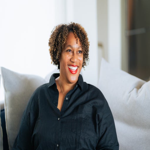 A guest with curly hair sits on a light couch, wearing a black shirt, in a sunlit room designed for comfort and relaxation.