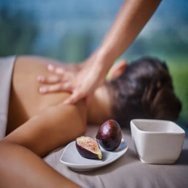 A guest enjoys a relaxing massage, lying face down, with fresh figs and a small white bowl arranged neatly on a plate in the foreground.