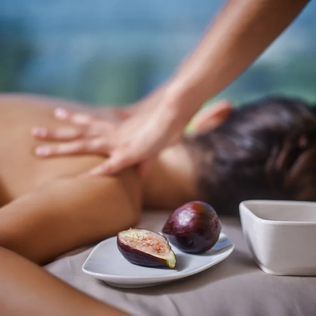 A guest enjoys a relaxing massage, lying face down, with fresh figs and a small white bowl arranged neatly on a plate in the foreground.