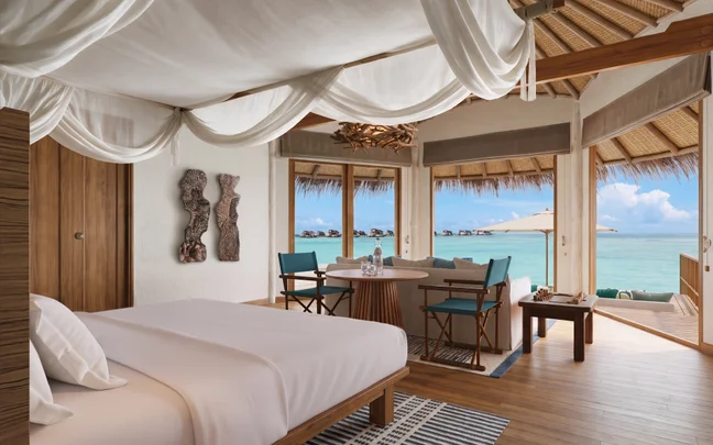 Bedroom in an overwater villa featuring a canopy bed, a seating area, and a deck with views of the ocean.
