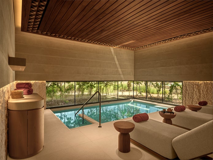 Spa room featuring an indoor pool, beige lounge chairs, rolled towels, wood ceiling, and a wide window with views of green landscape.