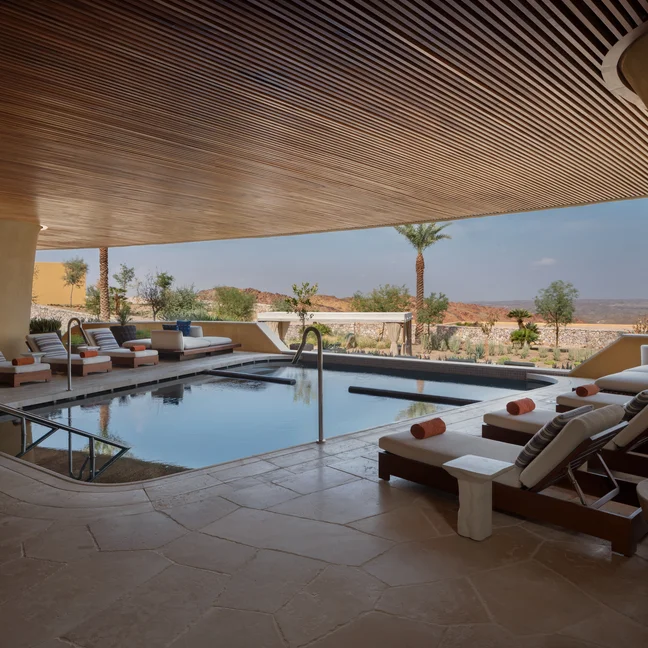 Indoor-outdoor pool area with lounge chairs, potted greenery, and warm wooden ceiling, open to palm trees and natural views for a relaxing and restorative atmosphere.