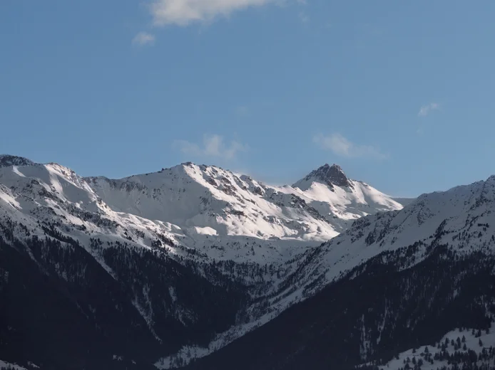 White peaks rise above a blue sky, while dense pine forests stretch along the lower slopes, reflecting the harmony of nature and tranquility of the surroundings.