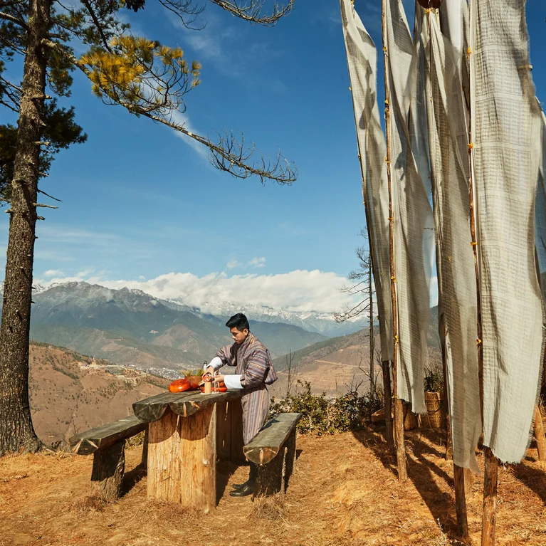 客人坐在木桌旁,欣赏着山景、高高的祈祷旗和湛蓝天空下的松树,感受着健康和与自然的和谐。.