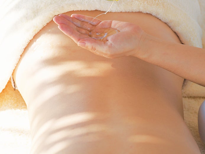 A therapist places massage oil in his hand beside a client lying face down on a massage table draped in a white towel.