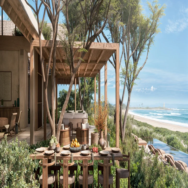 Dining table arranged for a meal on a shaded patio, with lounge chairs and abundant greenery overlooking the beach and ocean.