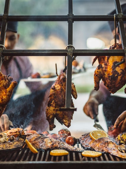 Chefs cook whole chickens, fish, and citrus halves over a charcoal fire.