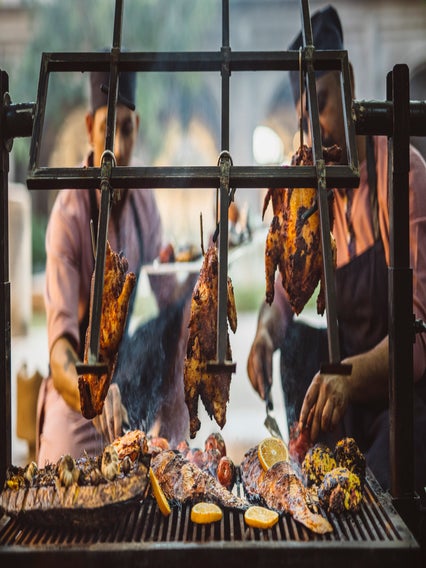 Chefs cook whole chickens, fish, and citrus halves over a charcoal fire.