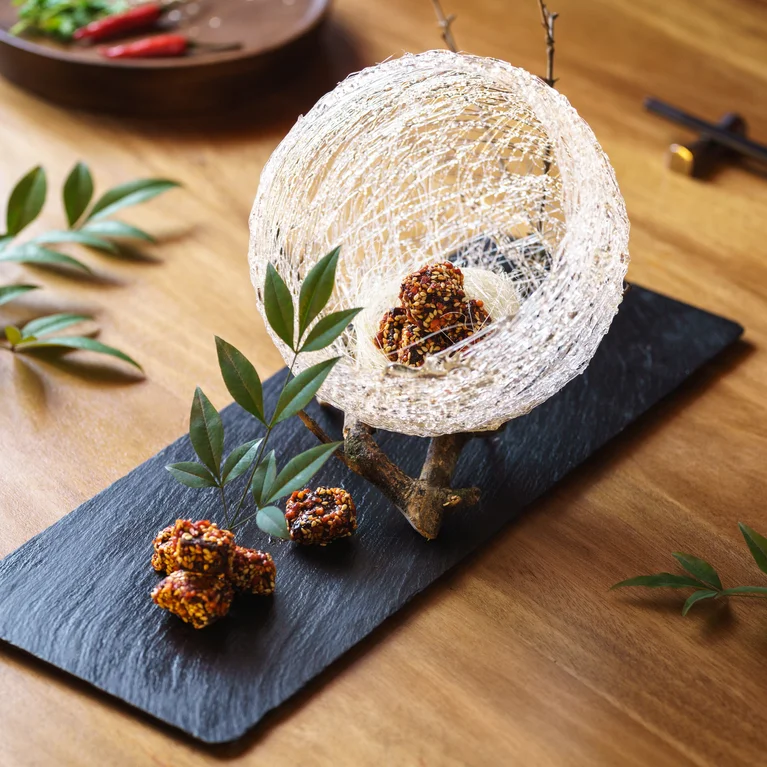 Bolas de azúcar en forma de huso sobre un plato de pizarra negra con golosinas de colores y verduras sobre una mesa de madera. Palillos y un plato de chile aparecen en el fondo. ...