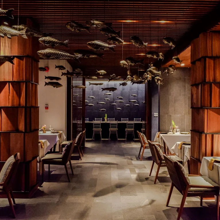 餐厅的内部装饰以天然木材为特色。餐桌摆放整齐,天花板上悬挂着鱼类雕塑,远处的墙壁上则陈列着鱼类雕塑。.