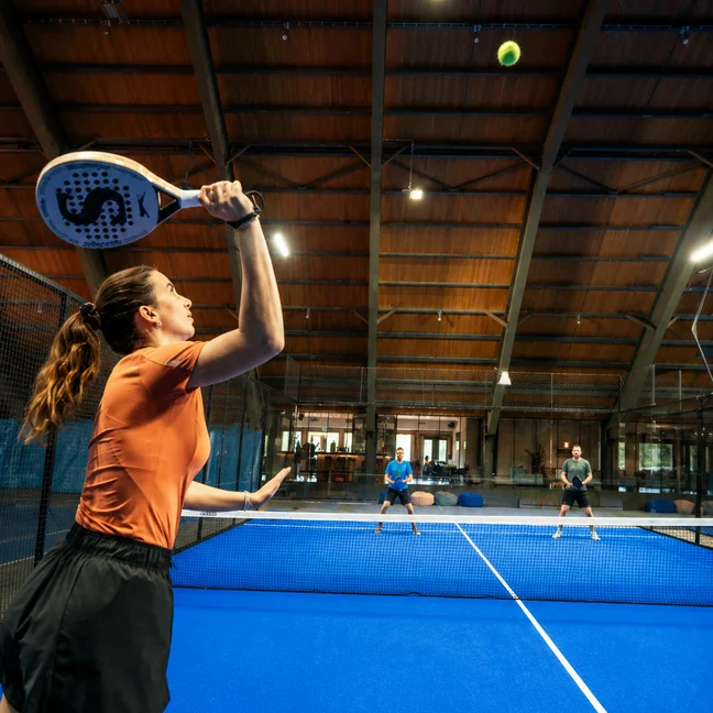 Un client en tenue de sport joue au padel sur un court couvert bleu, dans un cadre soigneusement conçu pour favoriser le bien-être et un mode de vie actif.