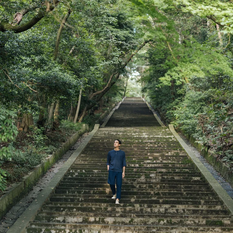広い石段は、静かな森の緑の木々の間を通り抜け、ウェルネスと環境調和につながる自然の中でのマインドフルな旅を誘う。.