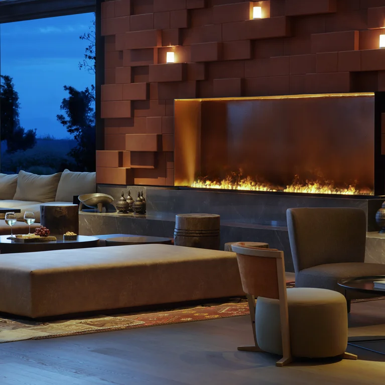 El salón cuenta con sofás de color beige, una alfombra estampada y una chimenea encastrada en una pared roja; una iluminación tenue realza el ambiente cálido y acogedor.