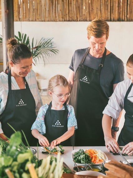 Invitados de todas las edades se reúnen en torno a la bien iluminada mesa de la cocina para preparar juntos ingredientes frescos en este moderno espacio. ....
