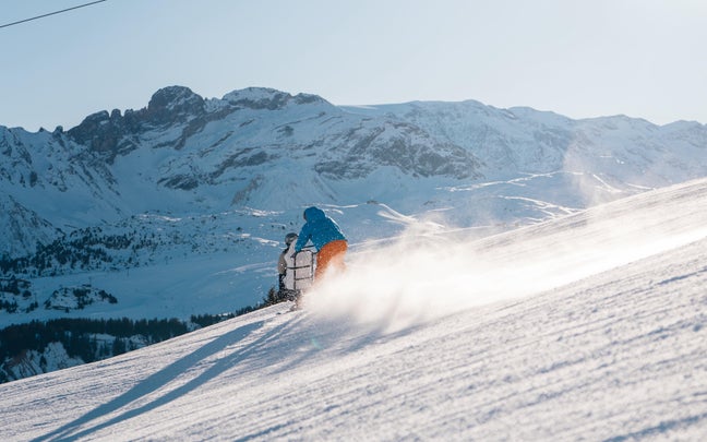 一名身穿蓝色夹克、橙色裤子的骑手正骑着雪地自行车从山坡上滑下。.