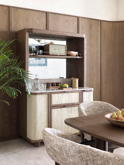 Dining room featuring natural wood walls, a cabinet displaying ceramics, greenery for ambiance, and a dining table with fresh pears arranged in a bowl.