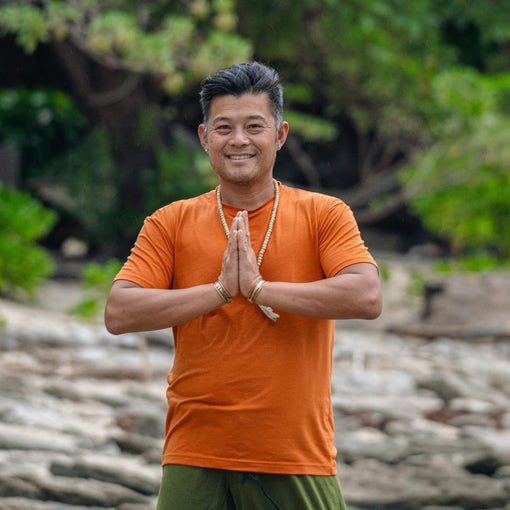 Guest outdoors, hands together in a gesture of gratitude, smiling amid natural greenery and stones. The setting reflects wellness and connection with nature.