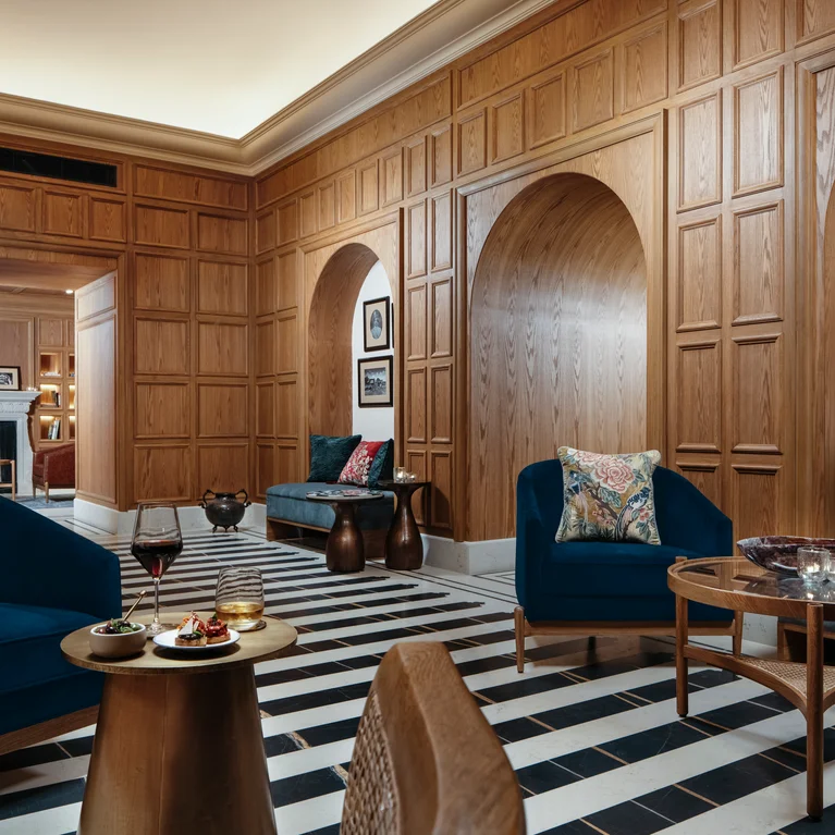 Inviting space with deep blue sofas, earth-toned pillows, natural wood walls, arched alcoves, and striped flooring. Relaxation tables and framed art create a welcoming setting.