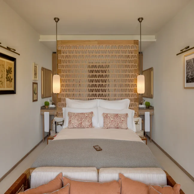 Bedroom with a large bed, patterned pillows, geometric accent wall, hanging pendant lamps, side tables with decor items, and framed artwork on neutral walls.