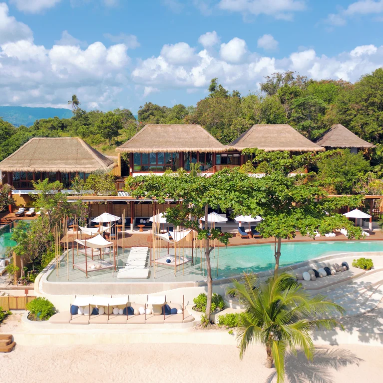 موقع على شاطئ البحر مع فيلات ذات أسقف من القش، وحوض سباحة واسع، وكراسي استلقاء للتشمس، وأشجار النخيل، وإطلالات شاملة على البحر والمساحات الخضراء المحيطة.