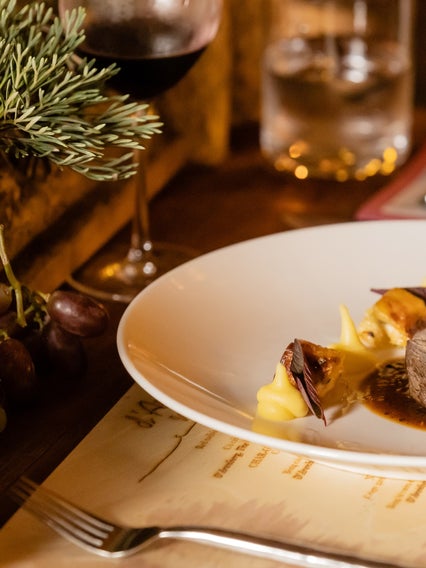 Steak, roasted vegetables and mashed potatoes served with gravy on a wooden table, accompanied by a glass of red wine and fresh grapes.