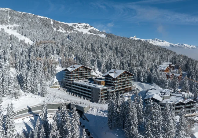 A contemporary resort harmonizes with snow-laden trees and mountain slopes, set beneath a clear sky, highlighting nature and mindful design.
