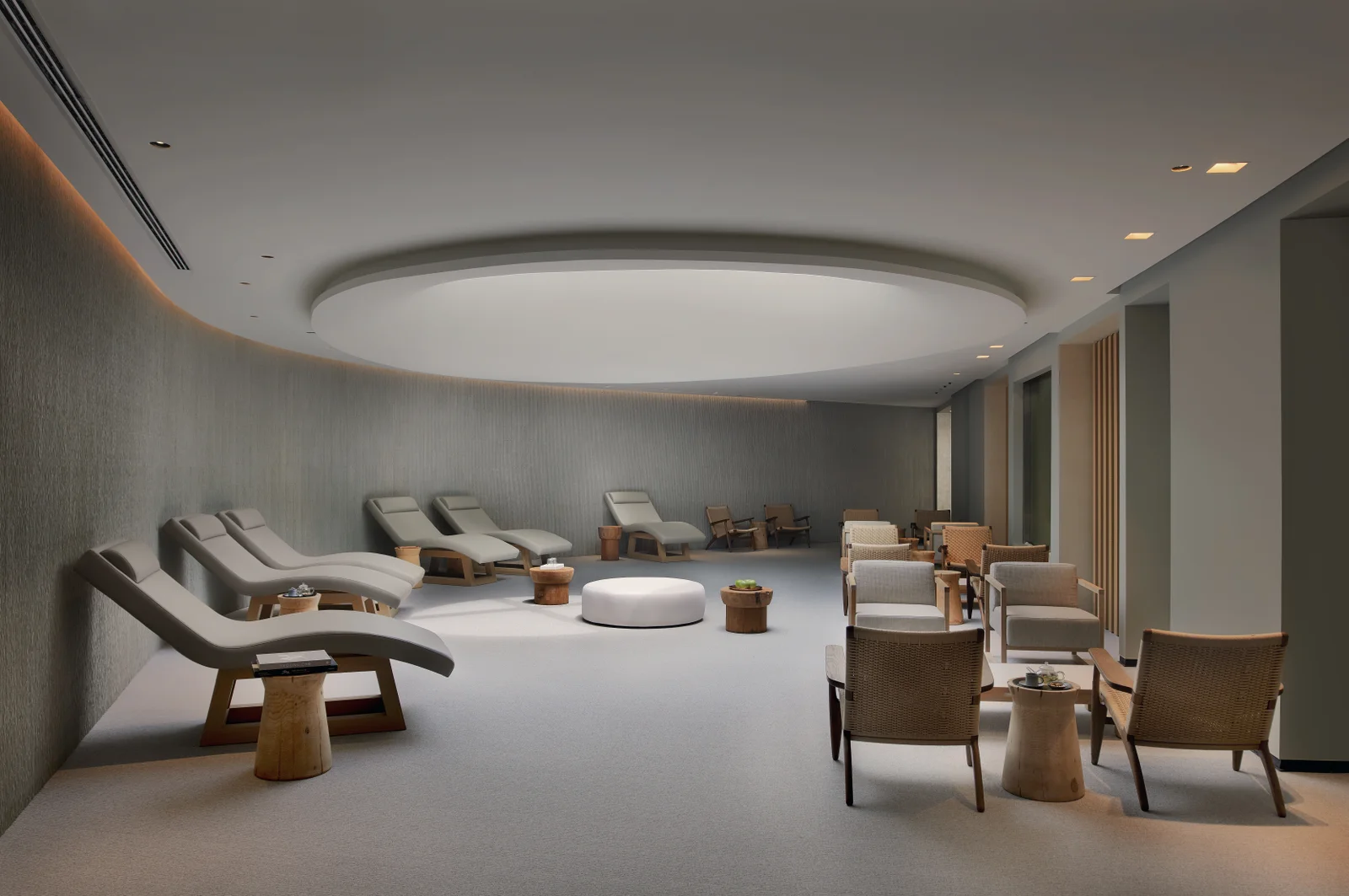 A relaxation lounge in grey and cream, curved loungers along one wall under an oval light panel and low armchairs grouped opposite.