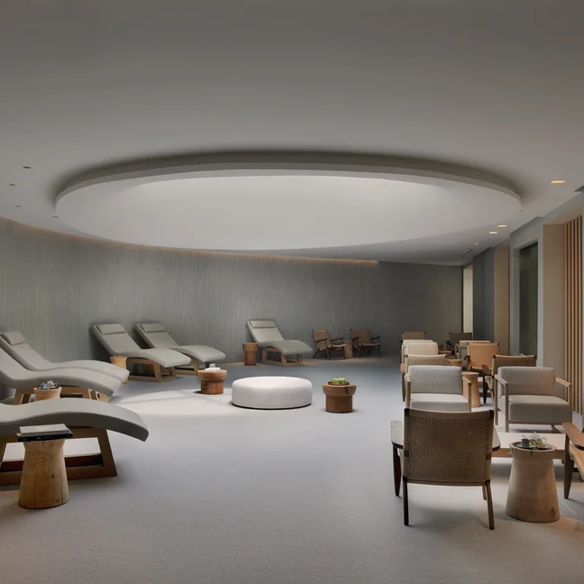 Curved-walled lounge with reclined chairs on one side, wicker seating with small tables opposite, and gentle light from a circular ceiling fixture.