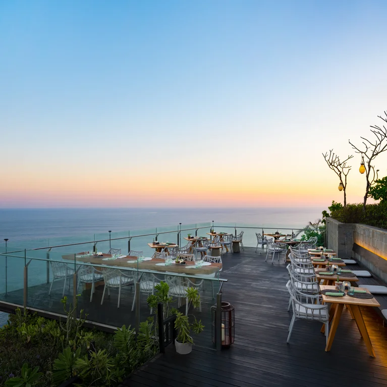 餐厅设有玻璃栏杆,黄昏时分可欣赏到海景;餐桌上摆放着现代感十足的椅子,露台上绿树成荫,营造出宁静自然的氛围。.