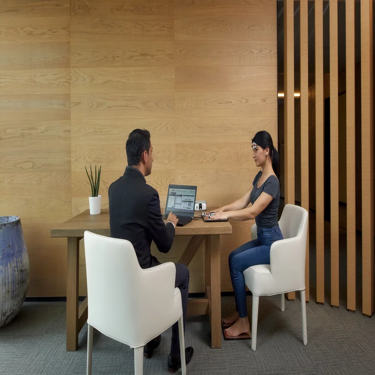 Colleagues collaborate at a natural wood table in a contemporary office, working on devices amid thoughtfully placed greenery and organized documents.