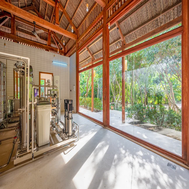 Sunlit room with floor-to-ceiling windows, indoor equipment on the left, and outdoor garden views that blend nature with thoughtful interior design.