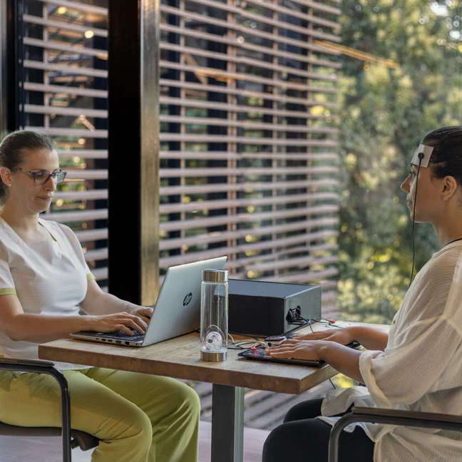 A guest enjoys a mindful technology experience as wellness sensors are gently placed, with natural greenery providing a calming backdrop through the window.