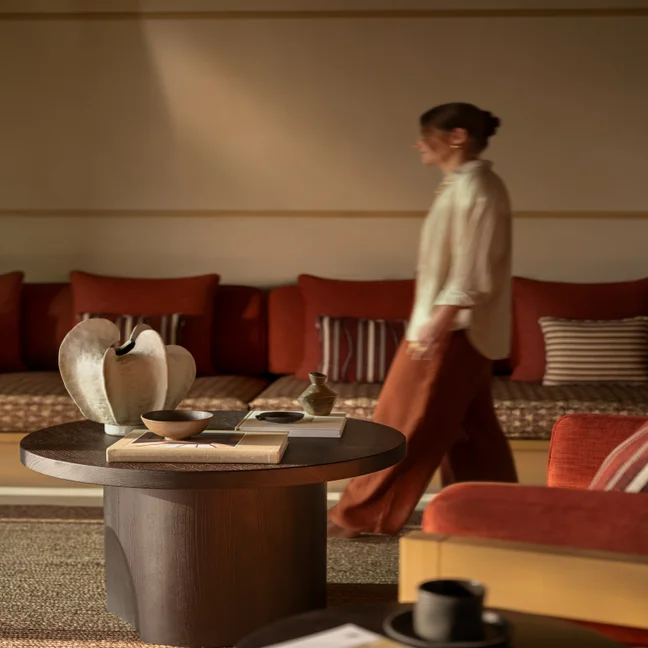A modern living room with warm-toned sofas, striped cushions, and a round wooden coffee table displaying curated decor and books.